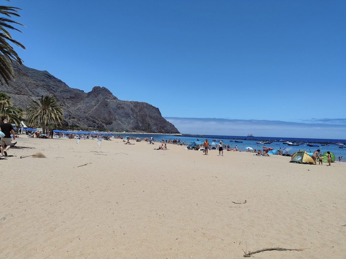 Rozległa złota plaża Playa de las Teresitas z palmami i ciemnymi górami Anaga w tle