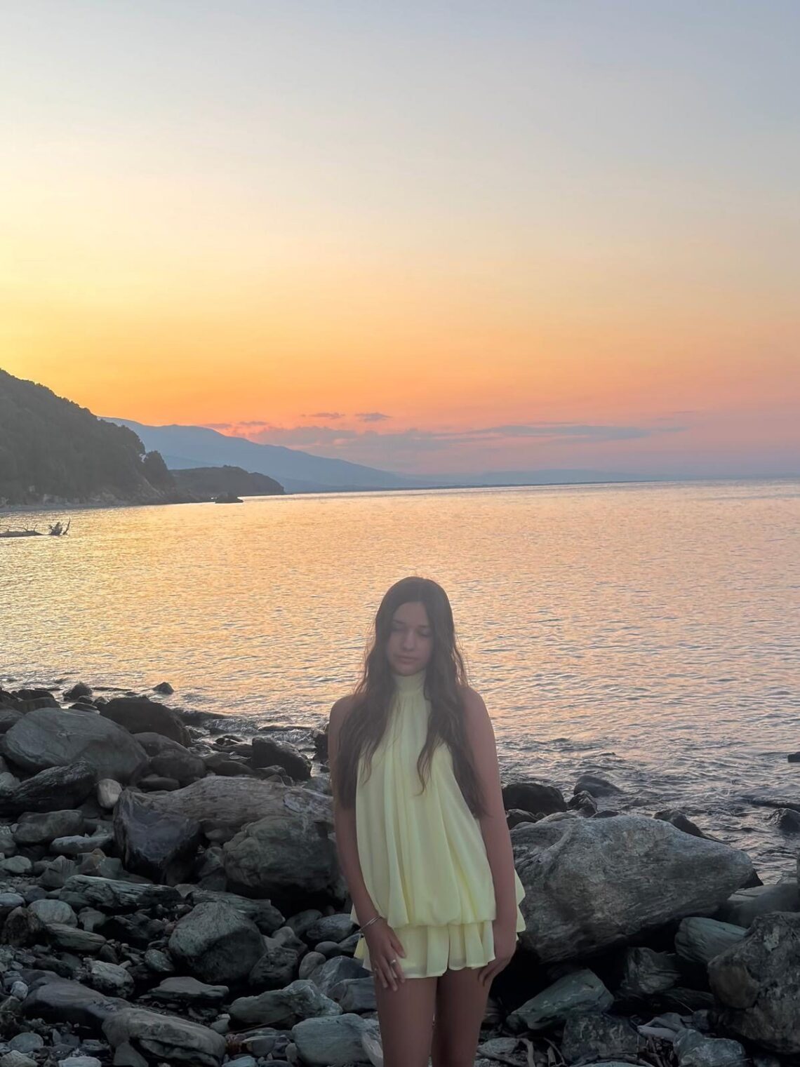 Marianna stojąca na skalistej plaży podczas złotego zachodu słońca w Kokkino Nero