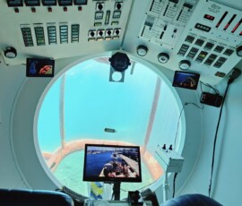 Wnętrze żółtej łodzi podwodnej – kokpit z bulajem Kokpit żółtej łodzi podwodnej z panelami sterowniczymi i okrągłym bulajem przez który widać dno oceanu