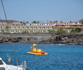 Żółta łódź podwodna przy porcie Costa Adeje Żółta łódź podwodna na błękitnej wodzie przy skalisto-piaszczystym wybrzeżu Costa Adeje
