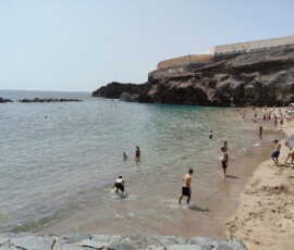 Playa de Abama – turyści w wodzie Turyści pływający w spokojnej turkusowej zatoczce Playa de Abama otoczonej wulkanicznymi skałami