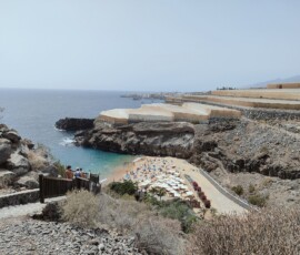 Playa de Abama – widok z klifu na zatoczkę Widok z klifu na turkusową zatoczkę Playa de Abama z plażą i leżakami oraz miastem w tle