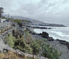 Puerto de la Cruz – kolorowe domy nad czarną plażą Kolorowe biało-żółte domy Puerto de la Cruz nad czarną skalistą plażą przy zachmurzonym niebie