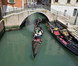 Mały kanał z gondolą pod mostem Gondola przepływająca pod kamiennym mostem w bocznym kanale Wenecji