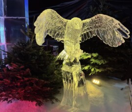 Hyde Park Winter Wonderland – rzeźba lodowa sowy Rzeźba lodowa sowy z rozpostartymi skrzydłami otoczona świerkami w Winter Wonderland