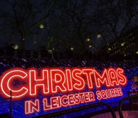 Leicester Square – neon CHRISTMAS IN LEICESTER SQUARE Neonowy napis Christmas in Leicester Square na niebieskim tle z drzewami z lampkami w nocy