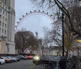 London Eye wieczorem – różowe iluminacje Koło widokowe London Eye z różowymi iluminacjami widziane z brukowanego zaułka wieczorem