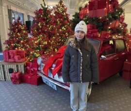 Marianna przy świątecznej dekoracji Harrods – czerwony Mini i choinka Marianna stojąca przed ozdobnym Mini Cooperem i ogromną choinką w holu Harrods