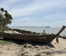 Krabi – drewniana łódka longtail na plaży Drewniana łódka longtail z tajskim napisem cumująca na piaszczystej plaży z widokiem na wyspy