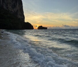 Krabi – zachód słońca na plaży ze skałami karst Fale rozbijające się o piaszczystą plażę Krabi z sylwetkami skał karst w blasku zachodzącego słońca
