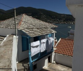 Dom z niebieskim balkonem i widokiem na zatokę – Skopelos Biały dom z niebieskim balkonem i praniem na tle zatoki w Chorze na Skopelos