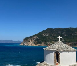 Kaplica z kamiennym dachem nad turkusową zatoką – Skopelos Biała kaplica z kamiennym dachem na tle turkusowej zatoki i zielonych wzgórz na Skopelos